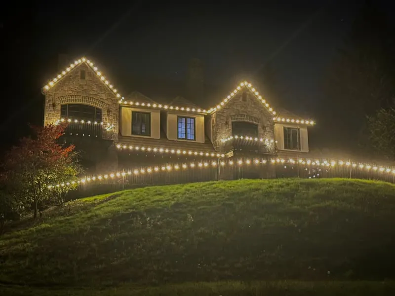 Stone house on a hill with warm white C9 bulbs along every roofline, balcony and fence